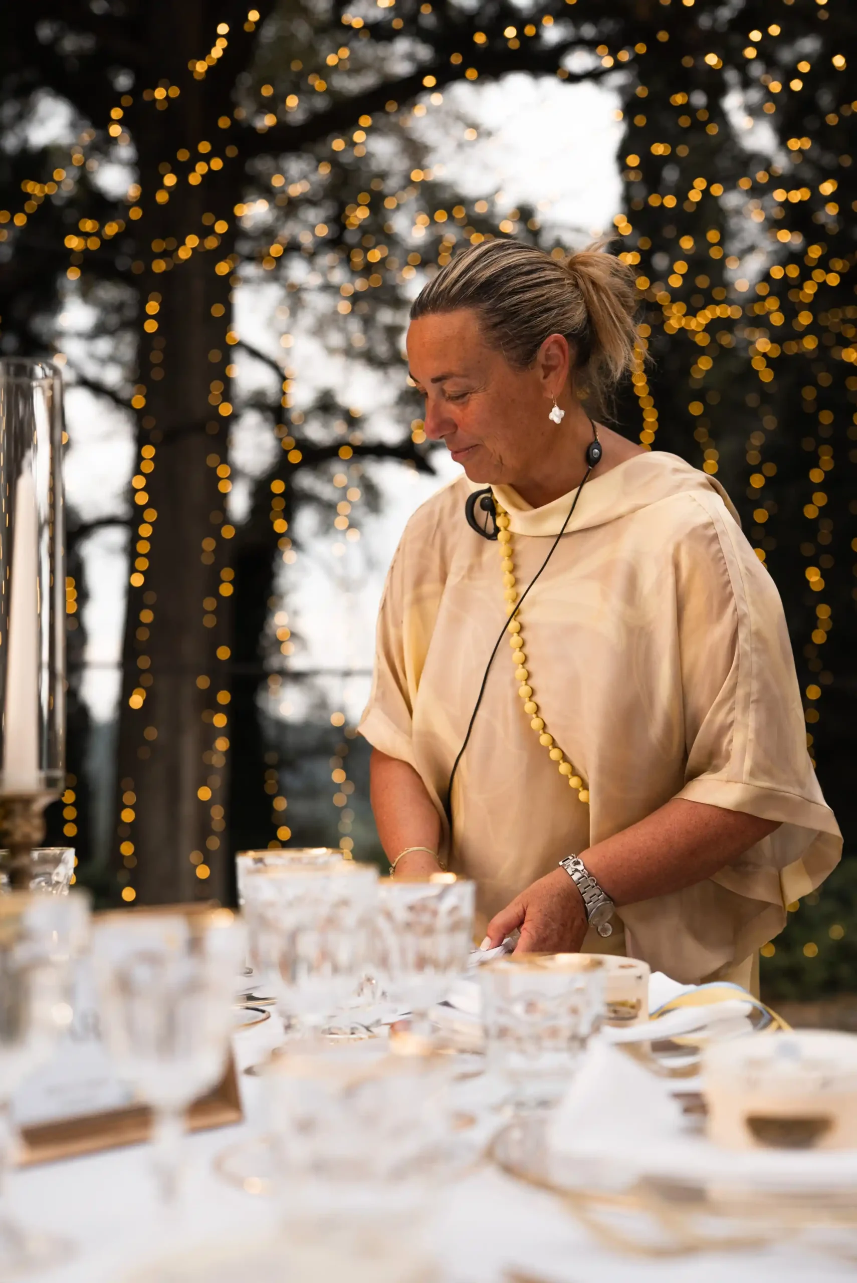 Donna sorridente che prepara dolci su tavoli decorati in location elegante con luci festose