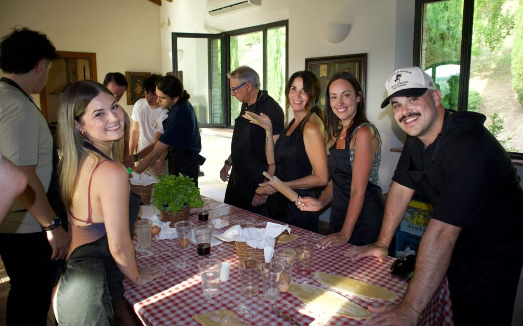 Gruppo di persone sorridenti in un evento conviviale con tavola imbandita in un ambiente rustico toscano