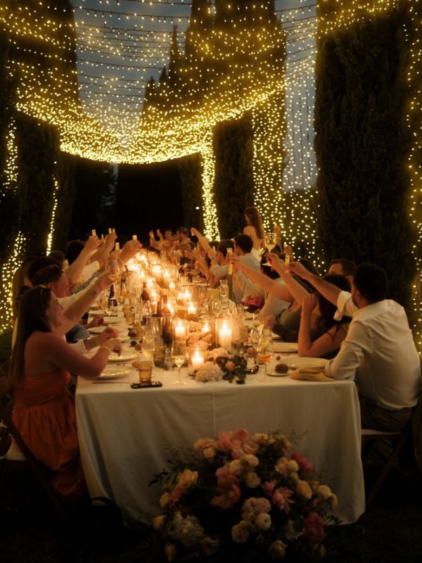 Matrimonio esclusivo in Toscana: cena romantica con ospiti che alzano i bicchieri in un ambiente illuminato da luci e candele